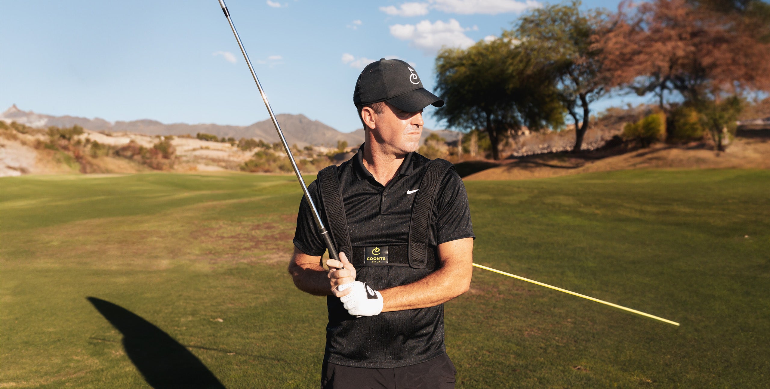 Tyler holding golf club on golf course with training aid harness on chest